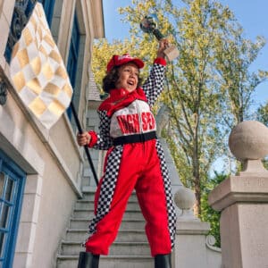 Rood-wit racer verkleedkostuum van Souza met pet – gedragen door een kind met finishvlag op de stoep voor een huis